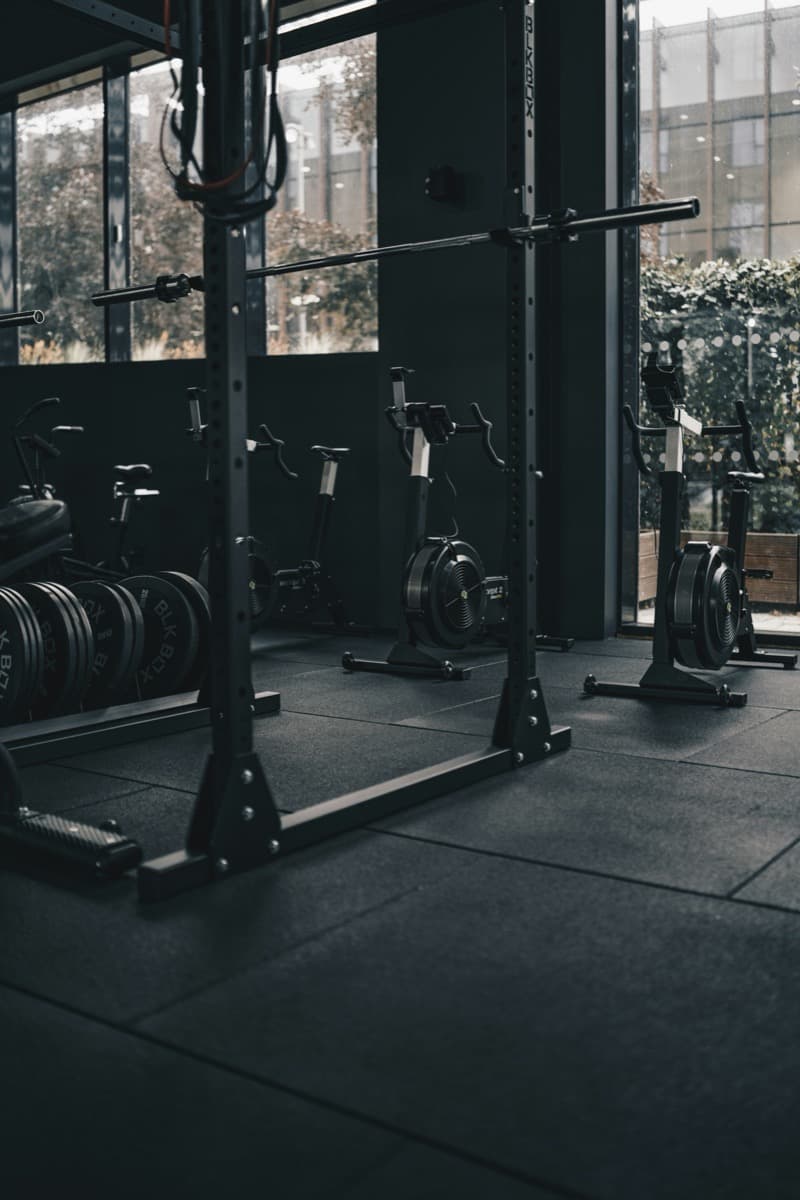 A compact building gym corner with a squat rack, weight plates, and exercise bikes