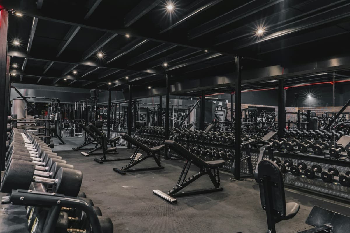 A large commercial gym floor lined with benches, dumbbell racks, and machines