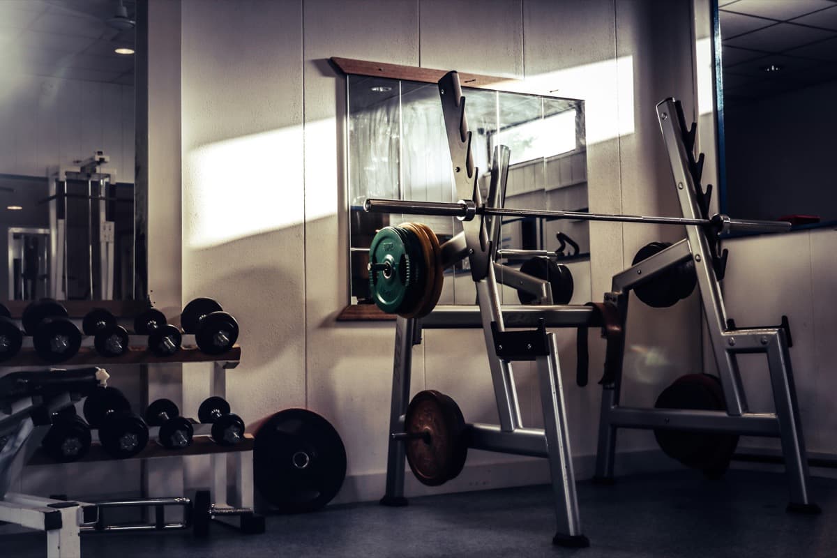 An old-school gym with a squat rack, mismatched plates, and a dumbbell rack