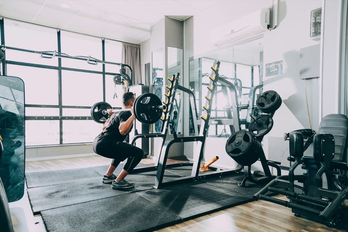 A small, bright hotel gym with mirrors, a squat rack, and weight plates